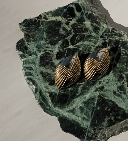 Pair of gold earrings on a green stone surface.
