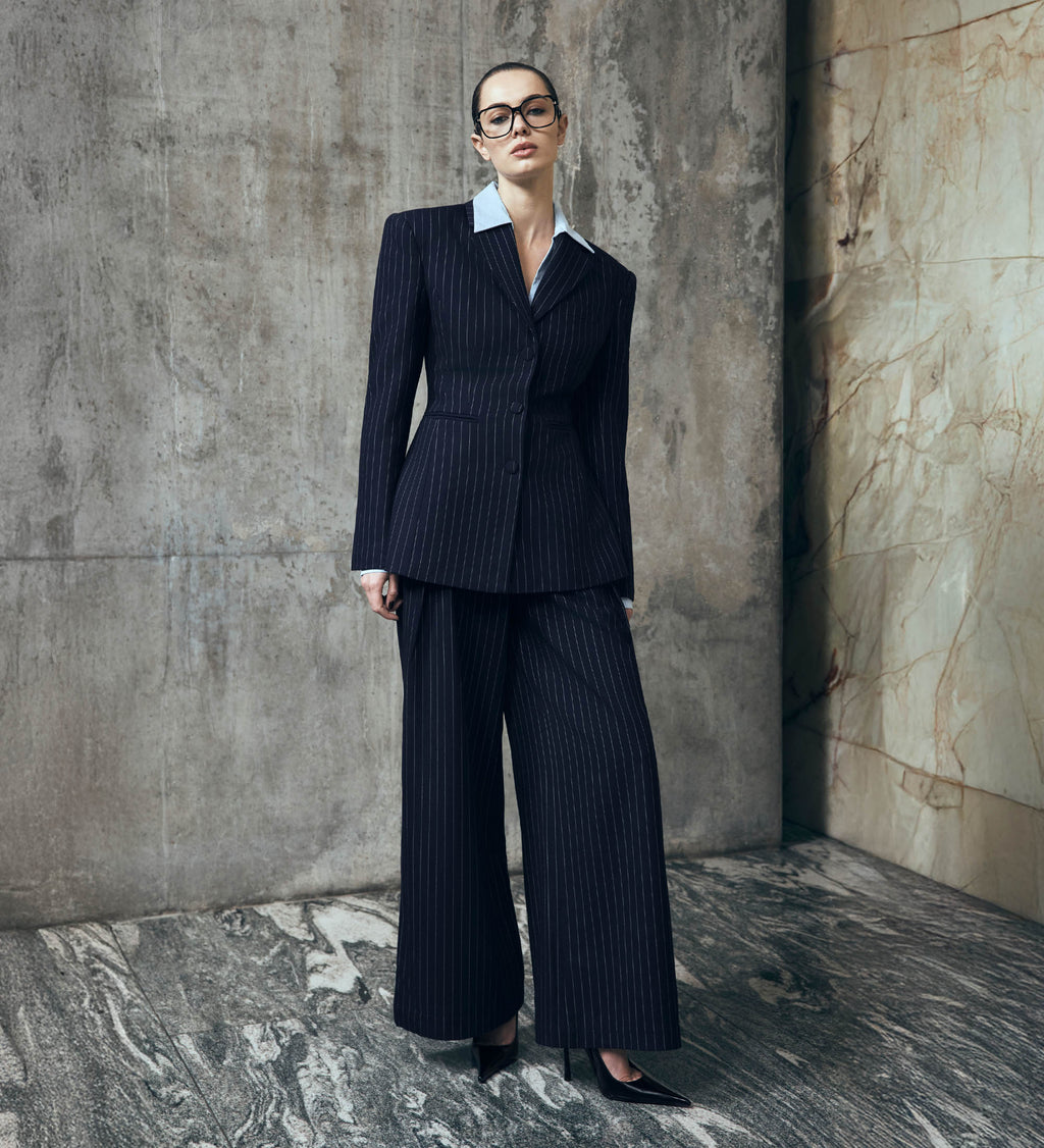 Woman in a navy pinstripe suit standing against a textured wall.