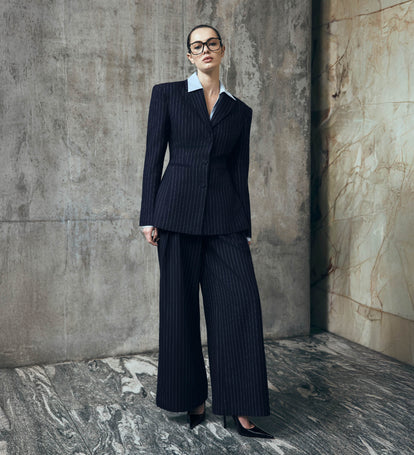 Woman in a navy pinstripe suit standing against a textured wall.
