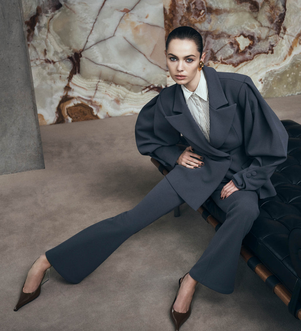Woman in a dark suit sitting on a couch against a marble wall.