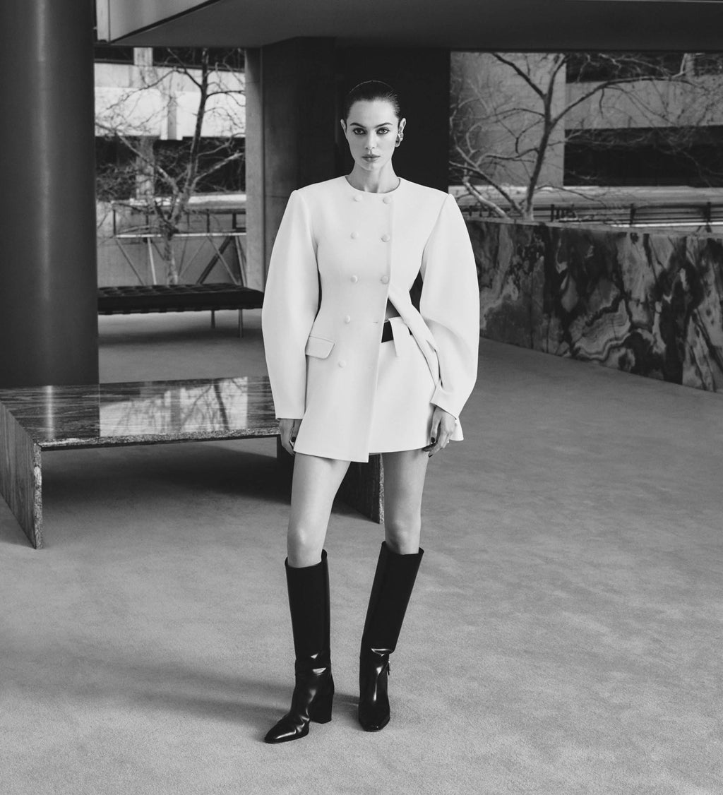 Person wearing a white outfit with black knee-high boots in an urban setting.