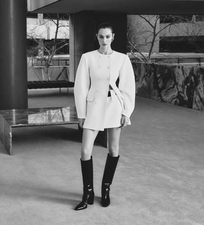 Person wearing a white outfit with black knee-high boots in an urban setting.