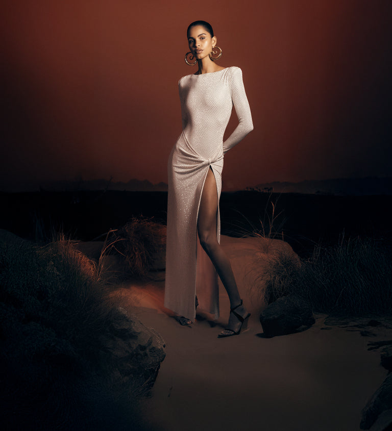 Woman in a white dress lying on sand with a desert landscape in the background.