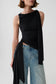 A model wearing a black draped sleeveless top with a side tie detail and light-wash blue jeans, photographed against a light gray studio background.