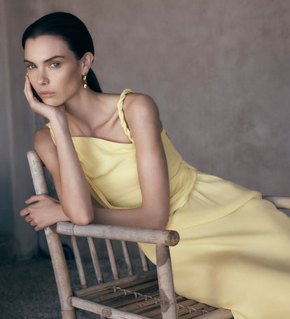 Woman in a yellow dress sitting on a wooden chair against a neutral background