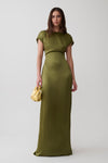 A woman modeling a floor-length olive green satin dress with short cap sleeves and a draped waist detail, holding a small metallic gold clutch against a light gray studio background.