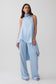 A model wearing a light blue sleeveless draped top and matching wide-leg pants, photographed against a plain light gray studio background.