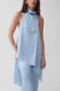 A model wearing a light blue high-neck draped top and matching light blue leggings against a plain light gray studio background.